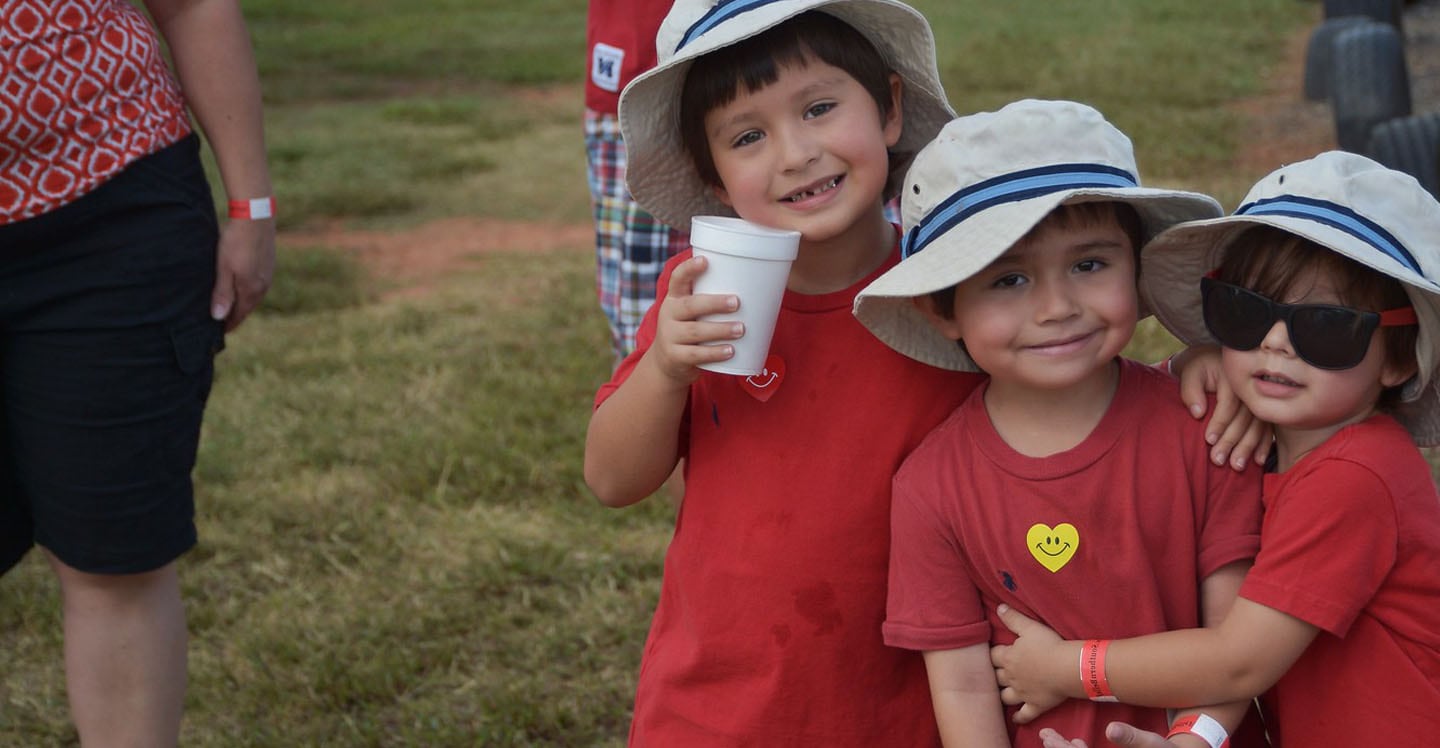 three boys wearing red shirts hugging outside