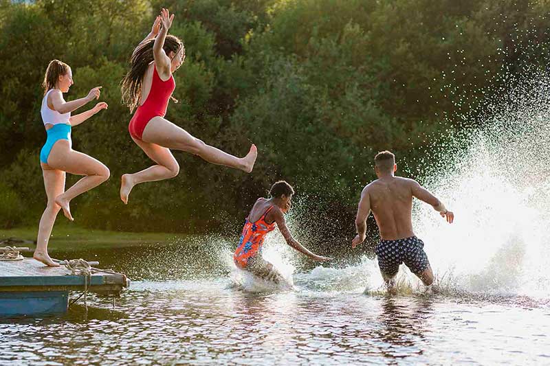 Teens jump off dock into river, practicing water safety to prevent drowning by swimming in a group.