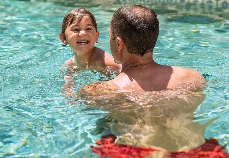 Dad uses touch supervision with toddler in the pool to practice water safety and drowning prevention.
