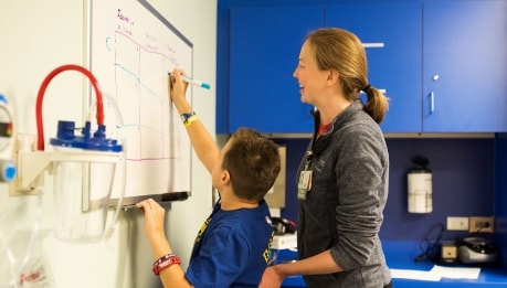 A child writes on a whiteboard with a speech pathologist at the Inpatient Rehabilitation Program