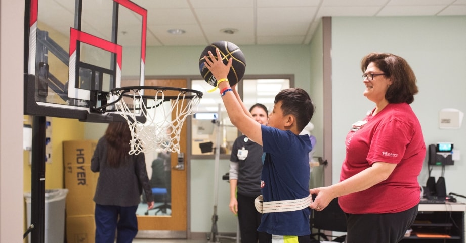 Clinician assists patient playing basketball in the Inpatient Rehabilitation Program