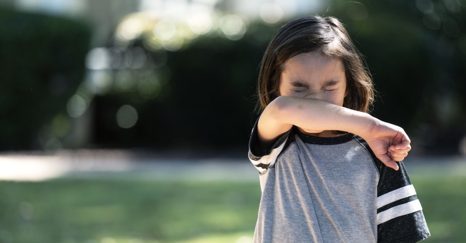 Young child coughing into elbow