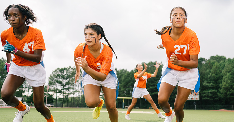Female teen flag football players running on a field.