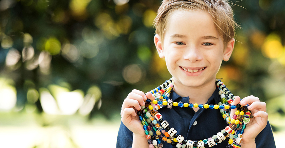 boy smiling outside holding a beaded necklace