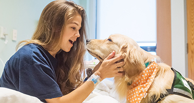 patient girl visits with therapy dog in pediatric hospital room