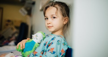 Patient girl holding stuffed animal with mask in pediatric hospital