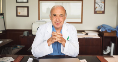 A pediatric neuro surgeon smiles at the camera sitting at his desk in his office