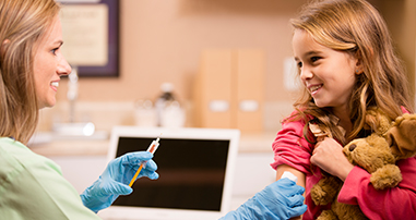 young girl holding teddy bear while getting flu shot