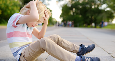 Young boy sitting on sidewalk holding head