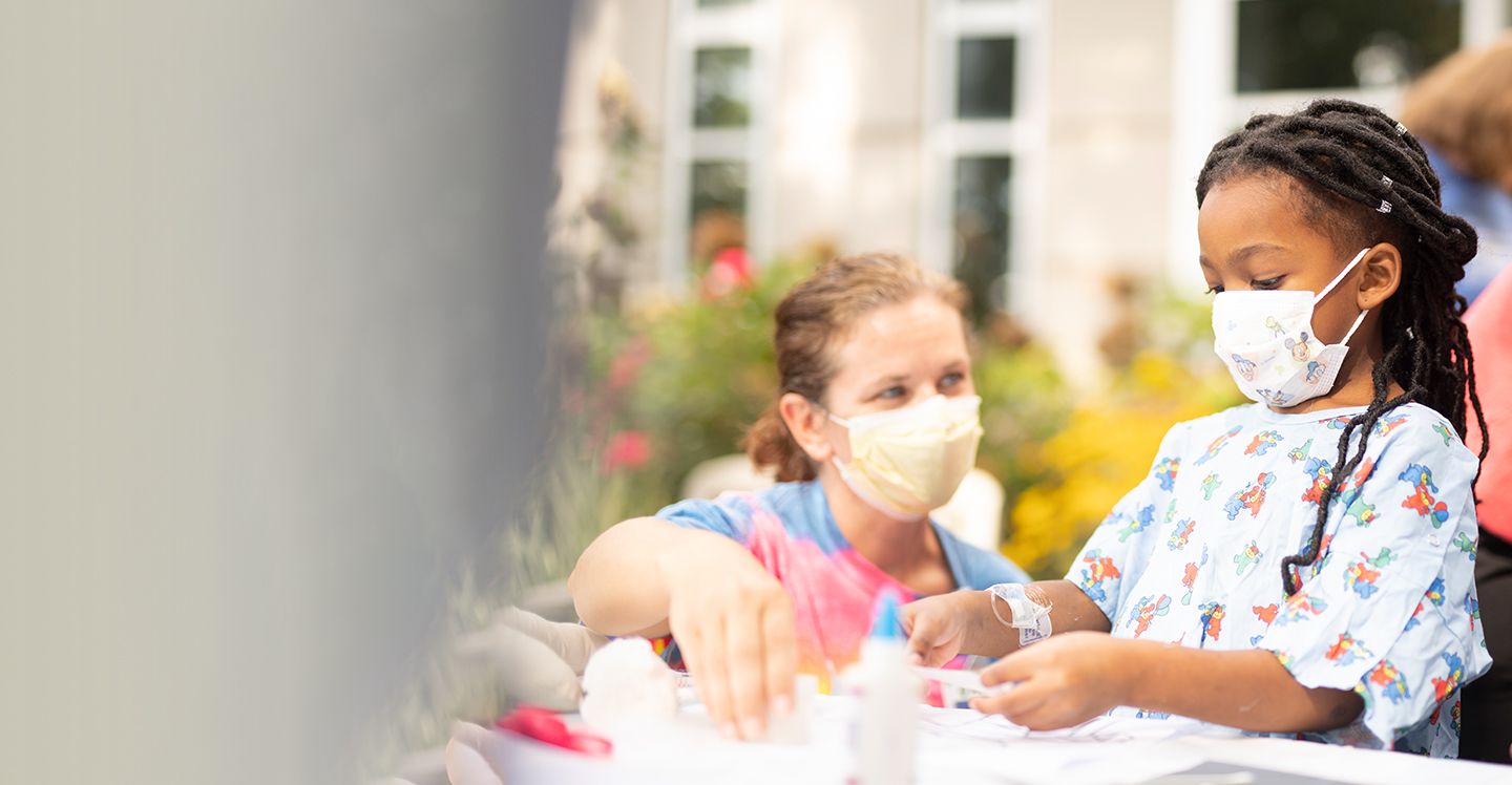 little girl patient doing crafts outside pediatric hospital with her nurse