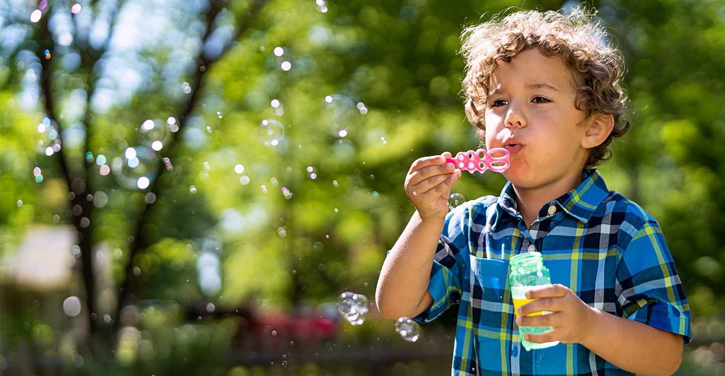 Toddler blowing bubbles in yard