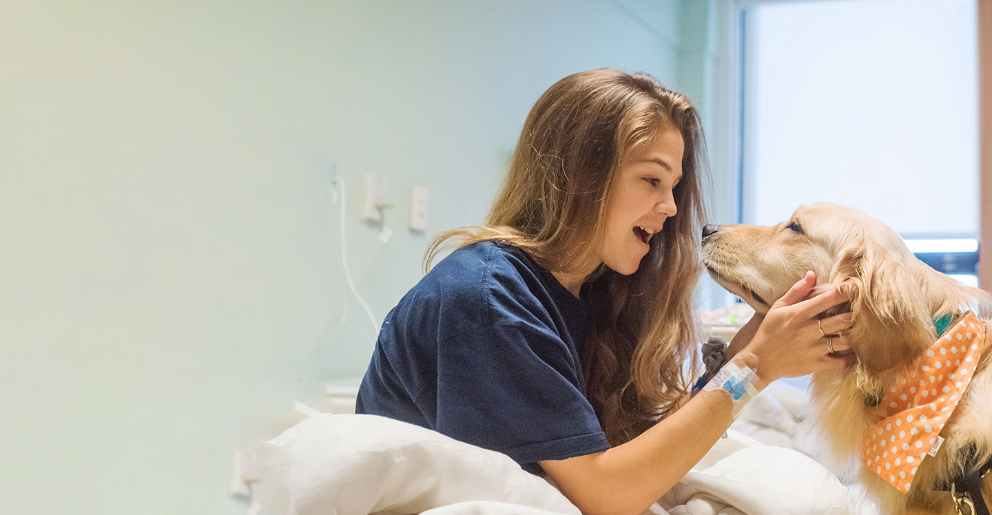 pediatric patient visiting with therapy dog in hospital bed