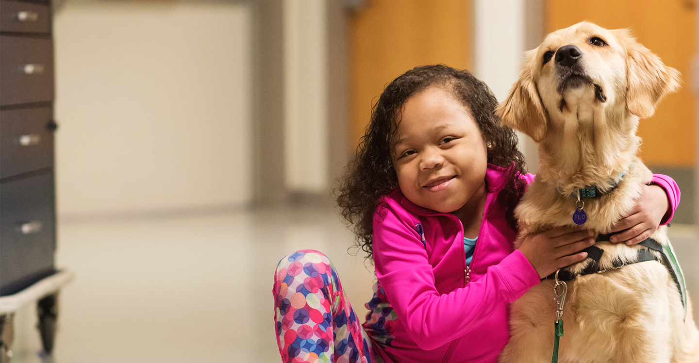Girl patient and canine therapy dog smiling in hallway of pediatric hospital