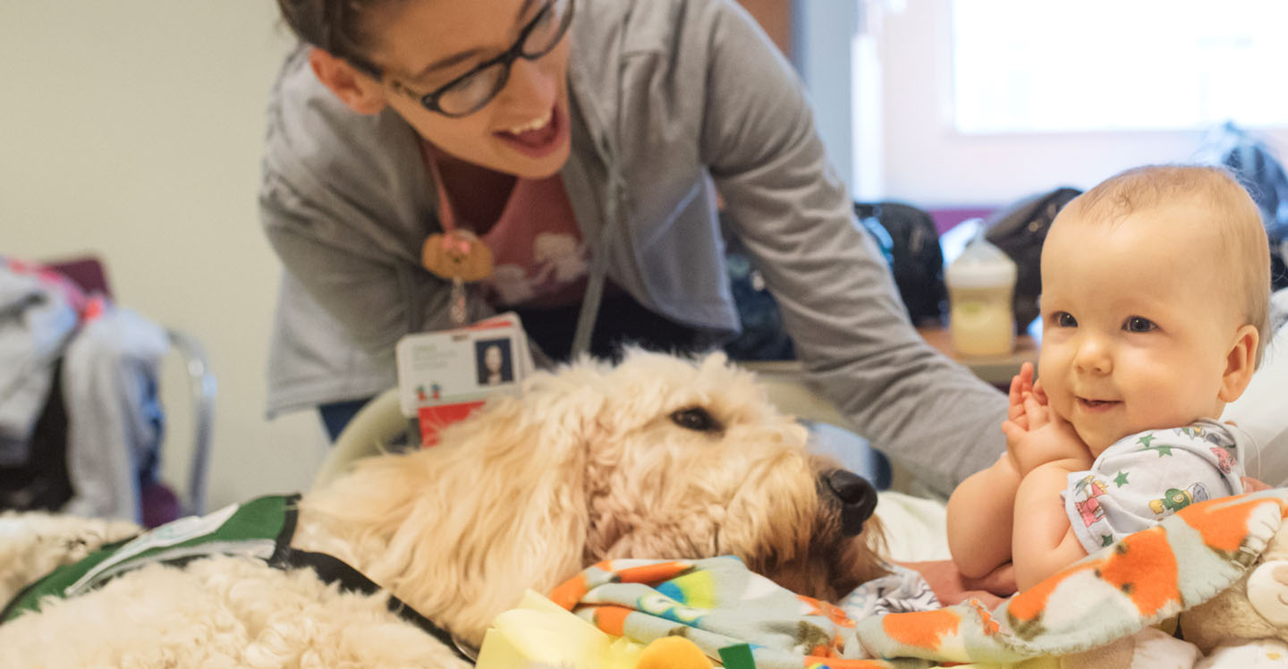 nurse with baby and therapy dog in hospital bed