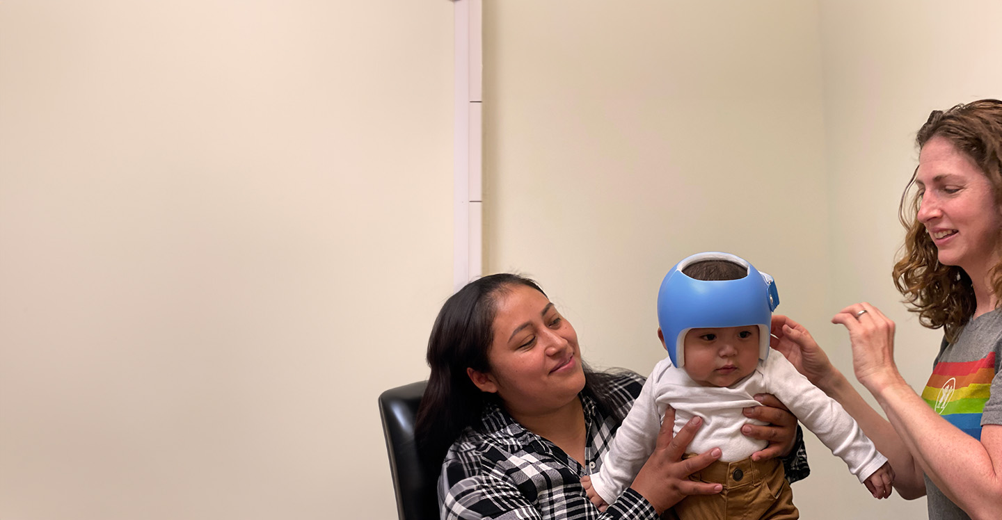 Baby with cranial remolding helmet in clinic with orthotist.