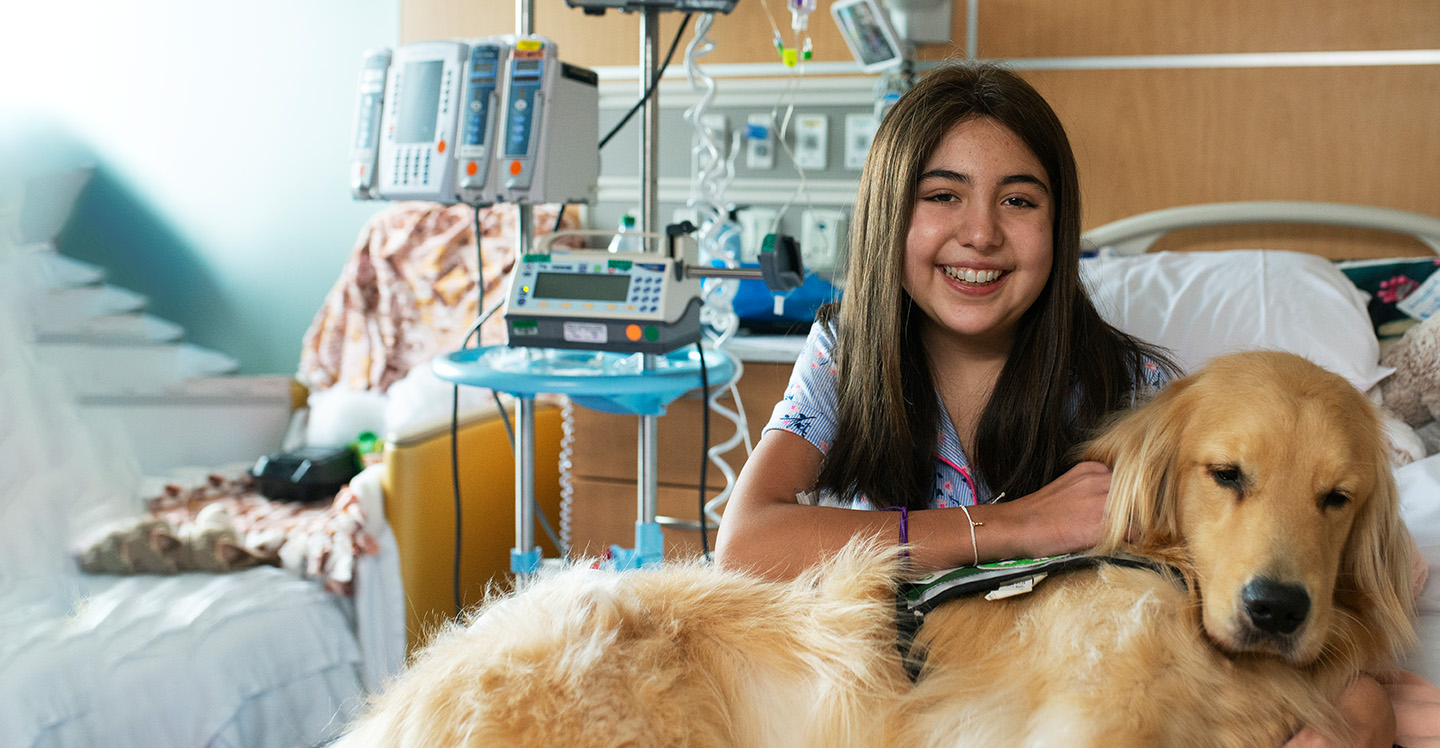 Pediatric cancer patient girl smiling hugging facility dog in her hospital bed