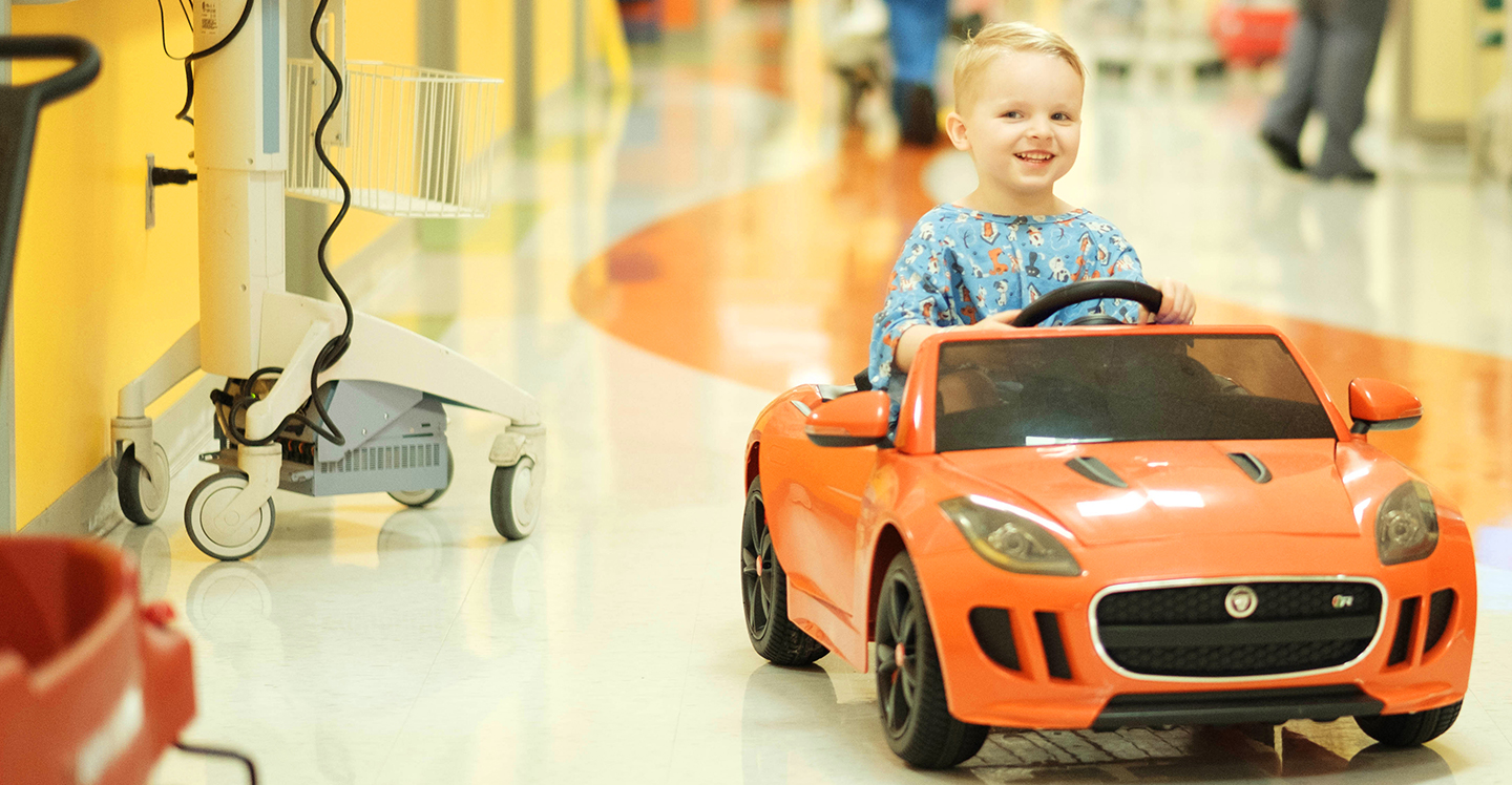 patient boy riding in toy car on the way to surgery