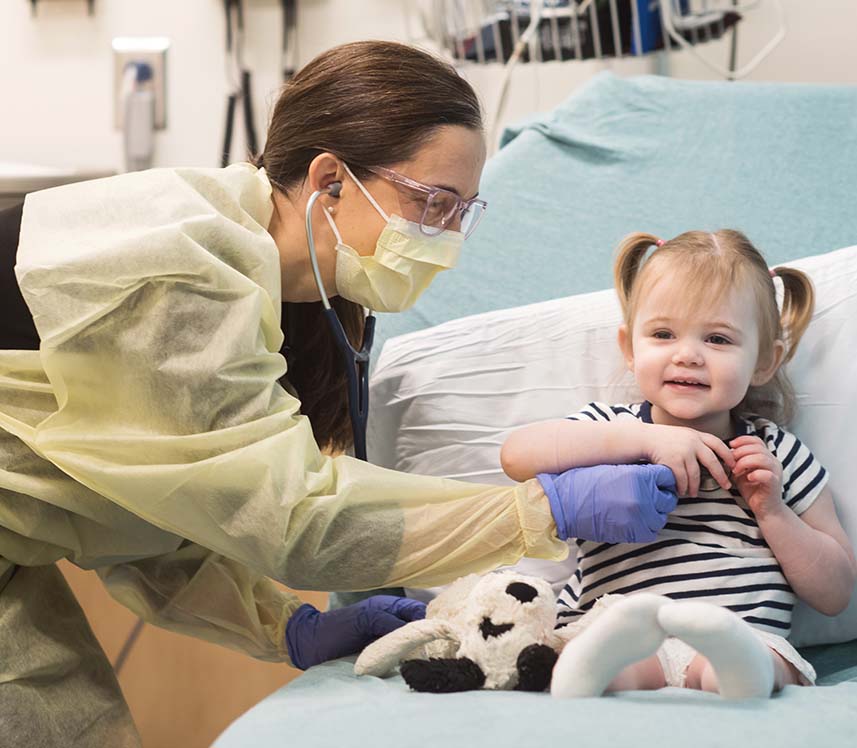 Little girl with pigtails smiling with nurse in pediatric hospital bed