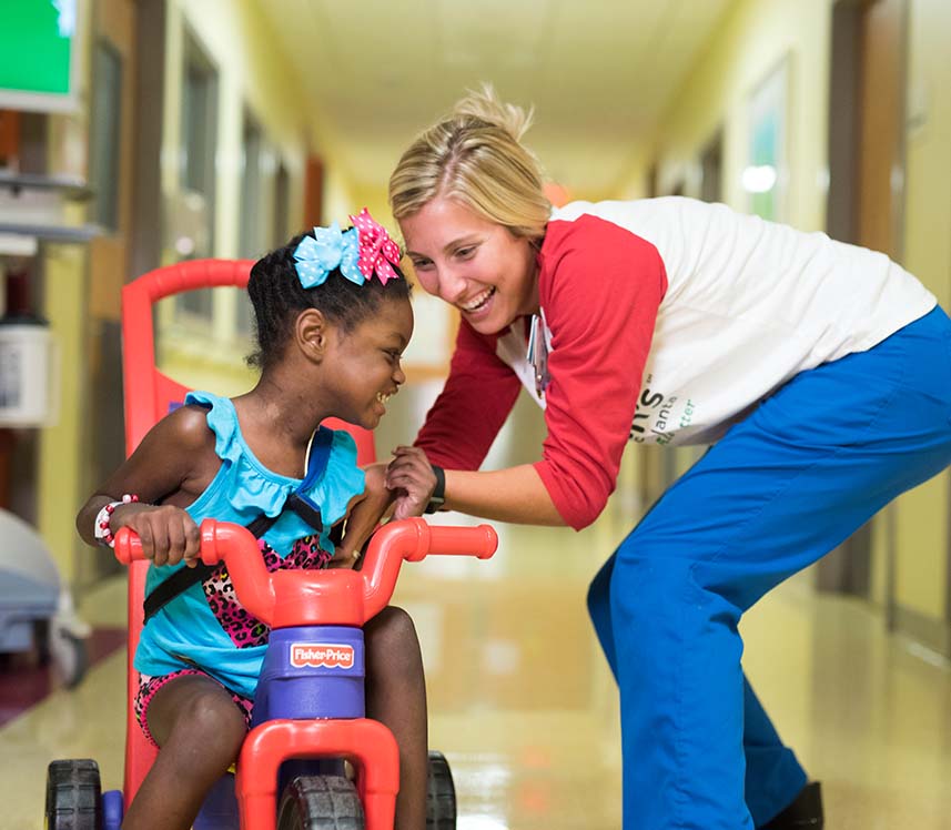 pediatric patient girl riding a bicycle in the halls of a hospital with her nurse