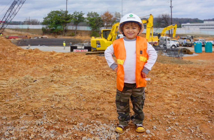 pediatric patient boy smiling at construction site wearing a hard hat