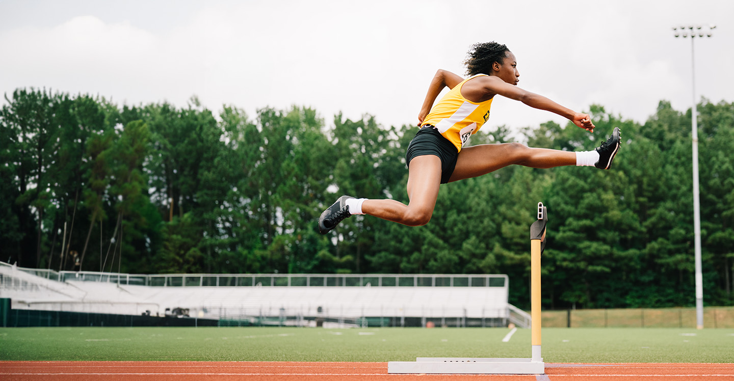 Female teen athlete jumps over hurdles on high school track